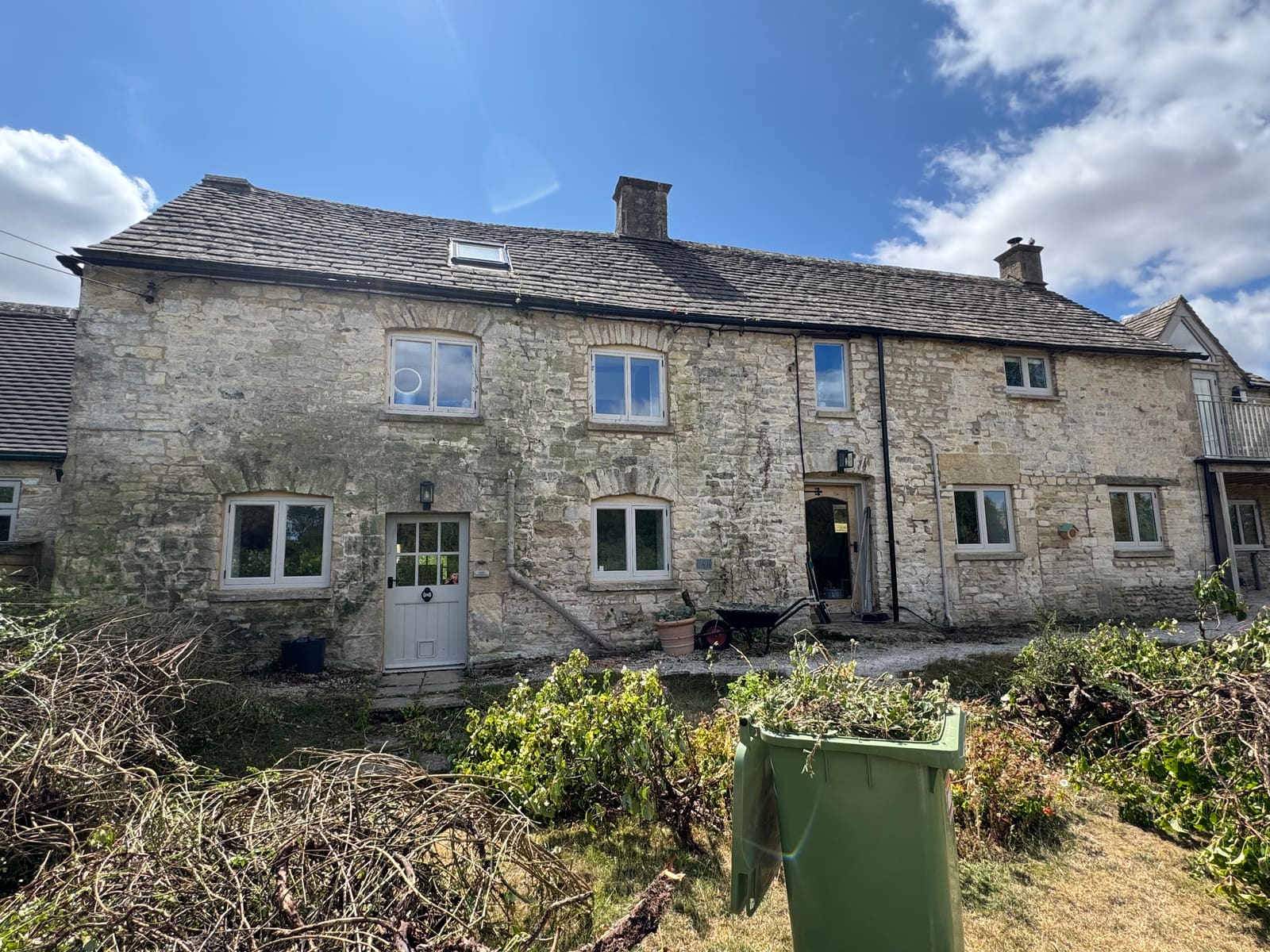 The front of the Cotswold stone cottage before the work, the stone dulled with green growth and the joints patchy with smeared grey mortar
