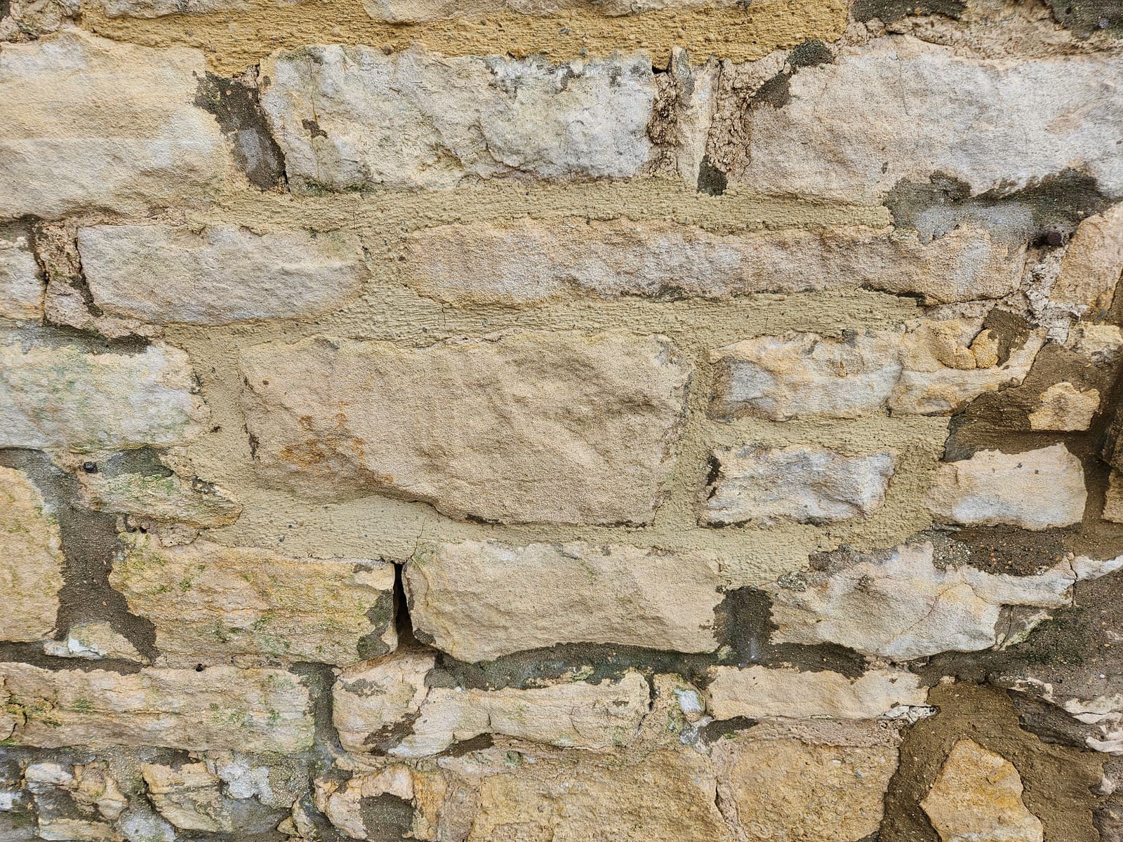 Close-up of the old pointing: grey cement patches smeared over the Cotswold stone, with an open crack between two stones