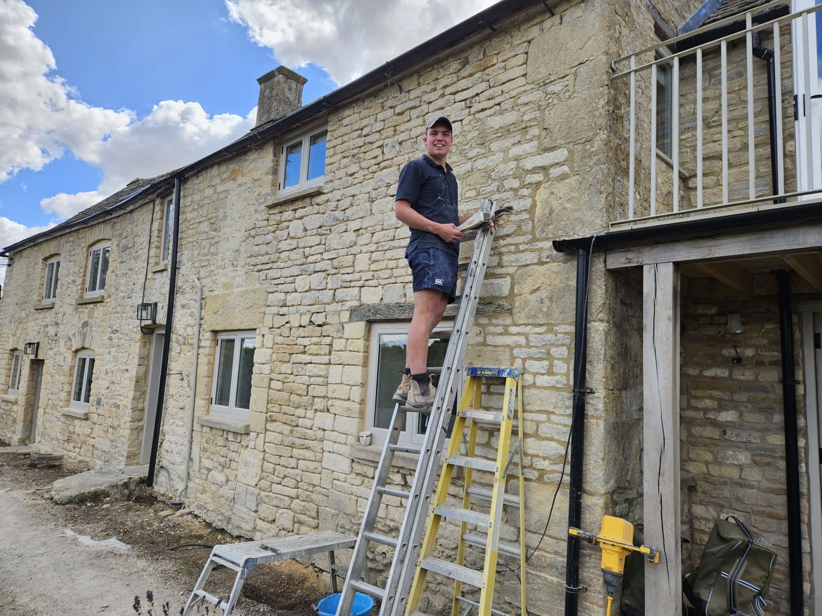 Charlie of Jackson's Stonemasonry on a ladder against the finished end wing of the cottage, holding a brush