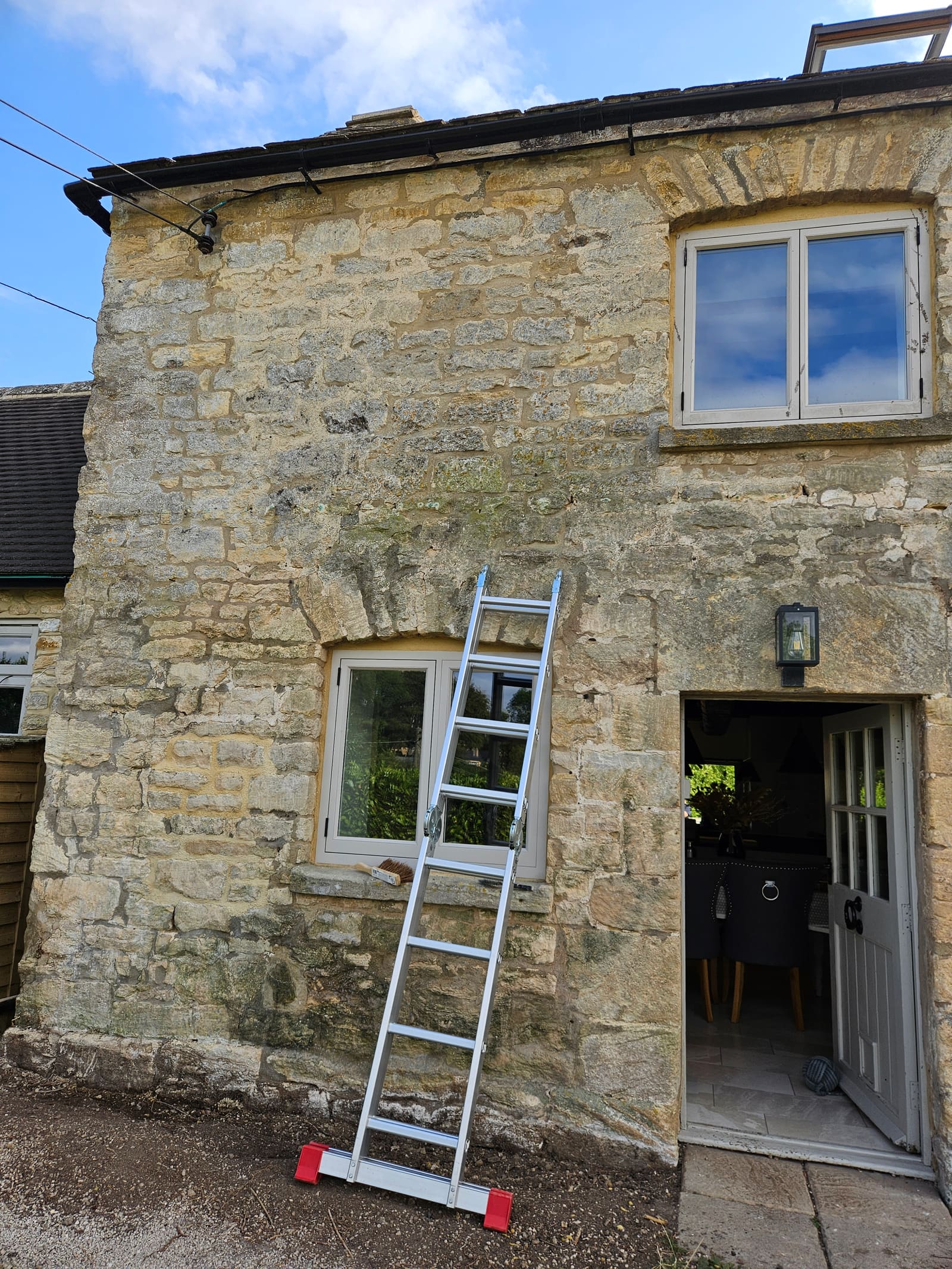 The end bay of the cottage before the work, with tired, uneven pointing and green staining along the base of the wall