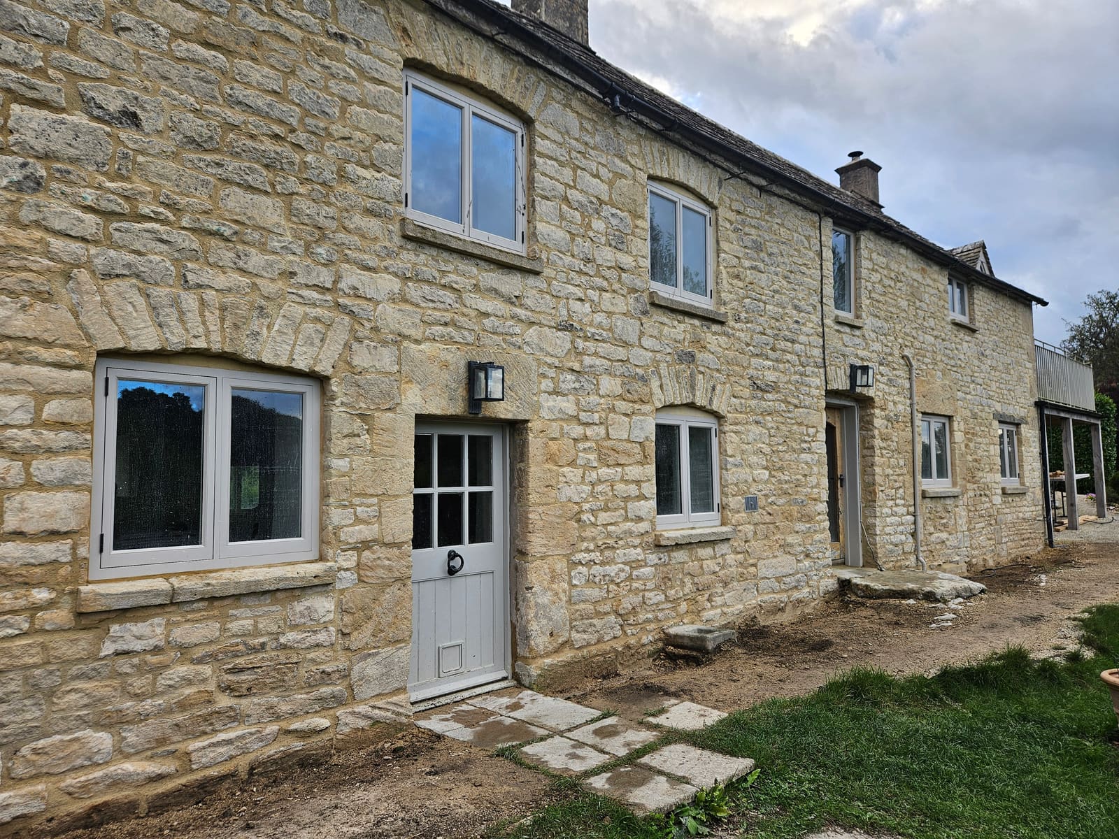 The finished front of the cottage seen at an angle, the stone evenly pointed in warm lime mortar around the windows and doors