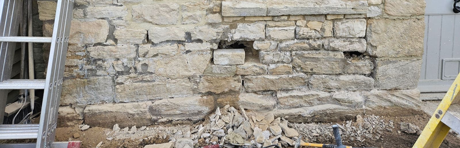 The wall below a ground-floor window opened up during the work, old mortar raked out and failed stones removed, with a pile of rubble at its foot