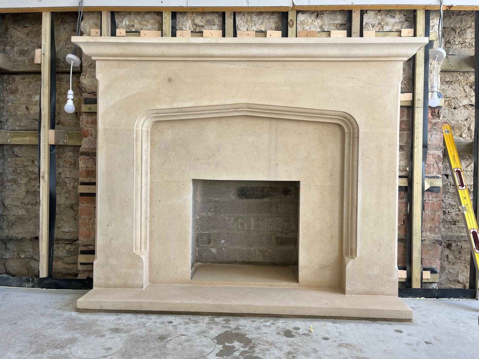 A limestone fireplace surround with a four-centred Tudor arch opening and a stepped mantel shelf, newly set against a stripped stone wall